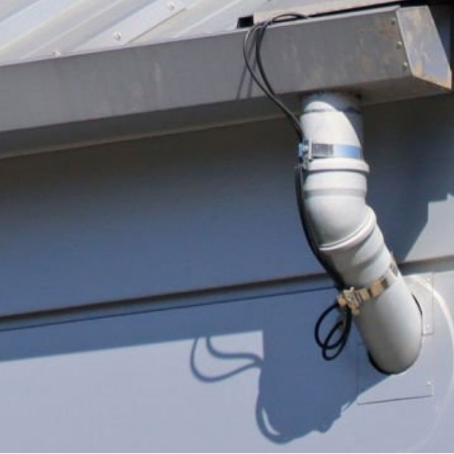 Close-up of Spartina seamless gutters and curved downspout connection on a commercial metal building in Athens, GA, with attached utility cables casting shadows on the wall.