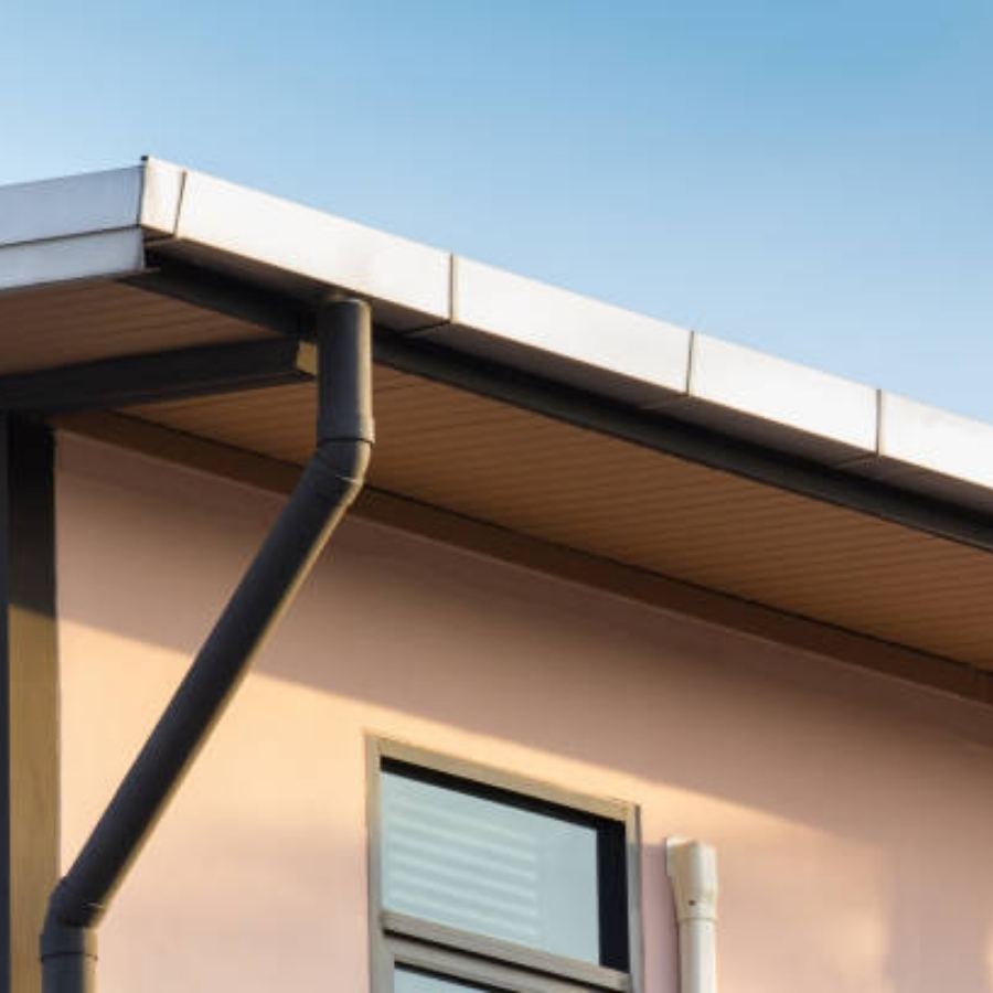Commercial building in Augusta, GA with Spartina seamless gutters and angled dark downspout along a flat metal roof above large windows, under a clear blue sky.