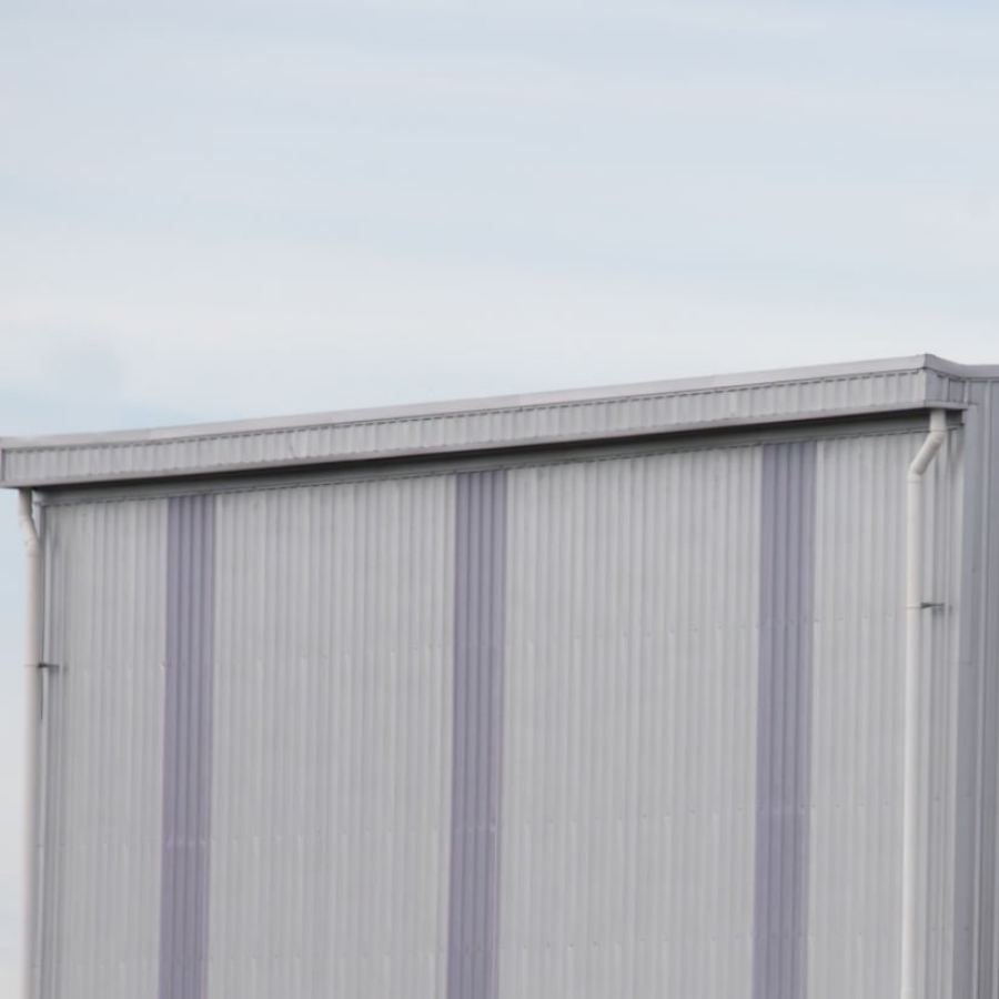 Large metal commercial building in Mount Pleasant, SC with Spartina seamless gutters and downspouts along the sloped roof, featuring vertical steel siding under a cloudy sky.