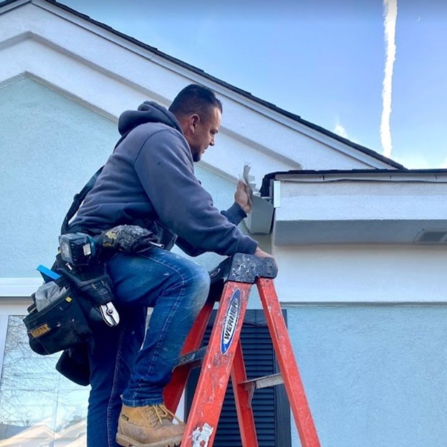 Gutter installation technician on ladder working on white seamless gutters on residential home in Port Wentworth GA for Spartina Seamless Gutters.