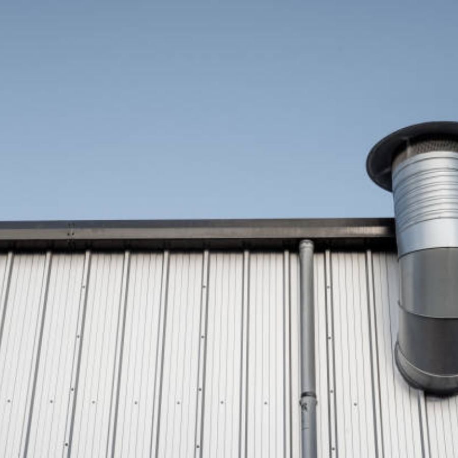 Industrial metal building in Rock Hill, SC featuring Spartina seamless gutters and a vertical downspout alongside a large rooftop vent against a clear blue sky.