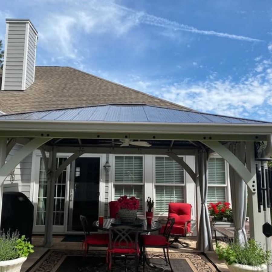 Backyard patio with covered pergola, metal roof, ceiling fan, white siding, seamless gutters, and outdoor dining furniture with red cushions in Skidaway Island GA by Spartina Seamless Gutters.