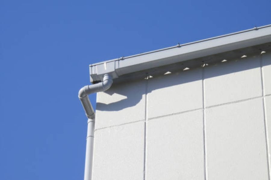 Commercial building in Atlanta, GA with light-colored Spartina seamless gutters and downspouts along the roof edge, set against a clear blue sky.