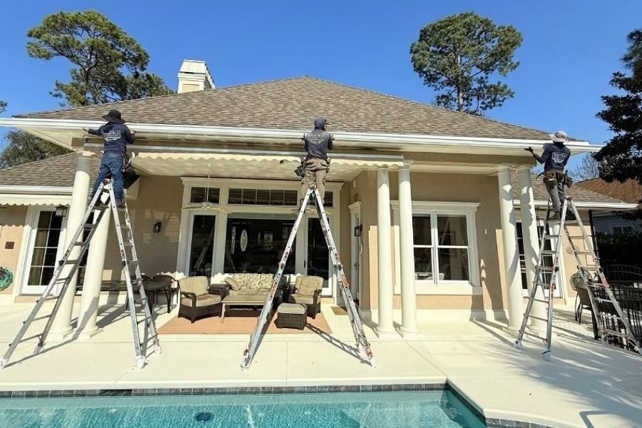Three professional gutter installers from Spartina Seamless Gutters installing new white seamless gutters on a luxury home with a swimming pool in Georgetown, GA.