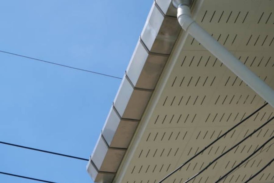Commercial building in Macon, GA with Spartina seamless gutters, soffit vents, and a white downspout along the roof edge under a clear blue sky with overhead utility lines.
