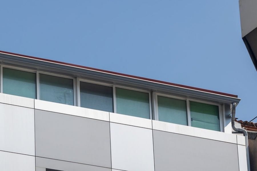 Modern commercial building in Mount Pleasant, SC with Spartina seamless gutters installed along the flat roof edge, featuring large windows and panel siding under a clear blue sky.