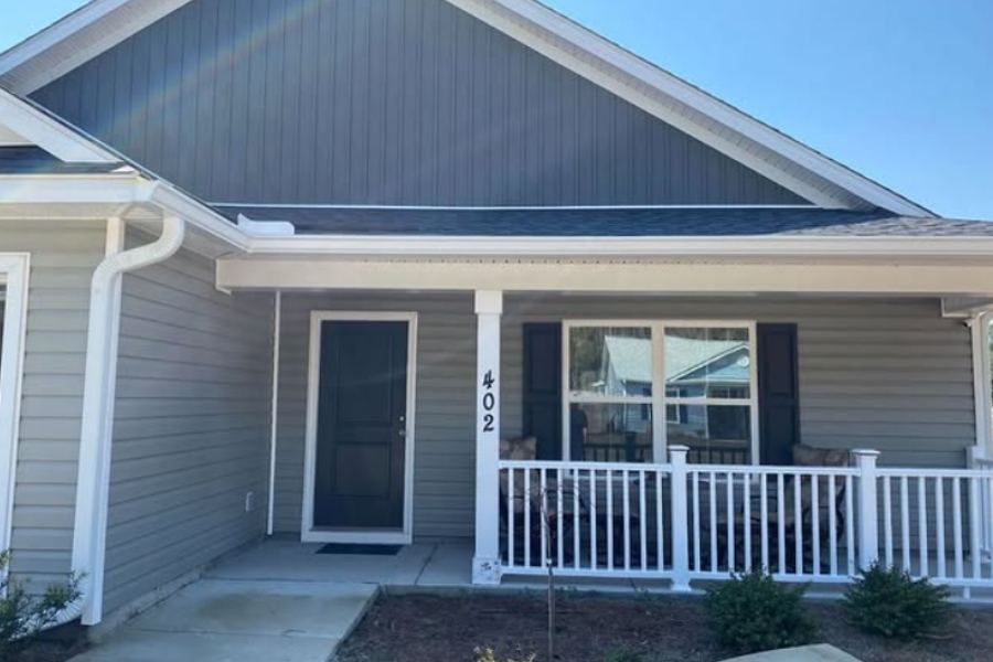 Front view of single-story gray siding home with white seamless gutters, covered front porch, white railing, and black front door in Port Wentworth GA by Spartina Seamless Gutters.