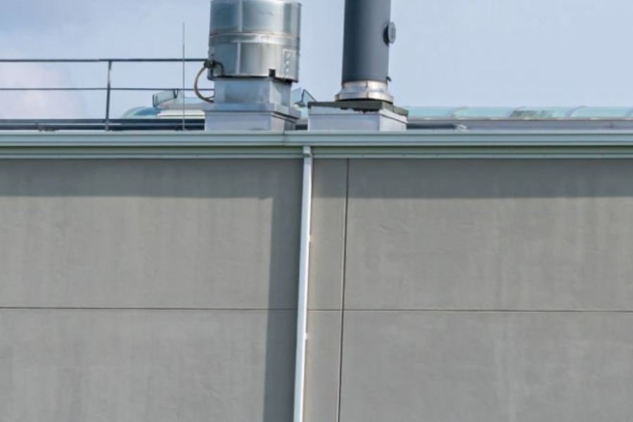 Industrial commercial building in Roswell, GA featuring Spartina seamless gutters and a vertical downspout on a flat, gray exterior wall with rooftop mechanical vents visible above the roofline.