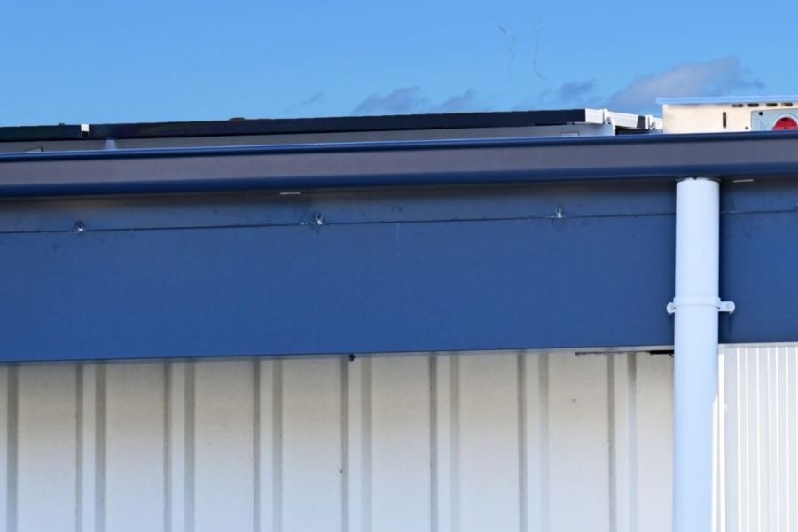 Commercial metal building in Savannah, GA featuring Spartina seamless gutters and a white downspout against blue trim and a bright sky.