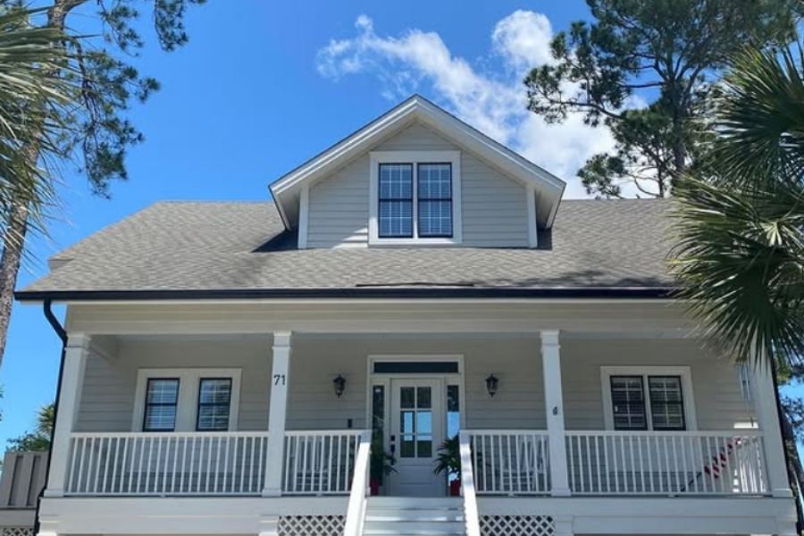 Two-story coastal-style home with large front porch, light gray siding, white trim, and seamless gutters under a blue sky on Skidaway Island GA by Spartina Seamless Gutters.