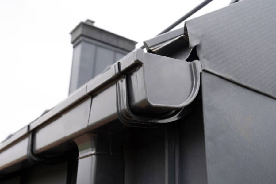 Close-up of dark-colored Spartina seamless gutters on a commercial building in Summerville, SC, showing corner detail and downspout connection against a modern metal roof and siding.