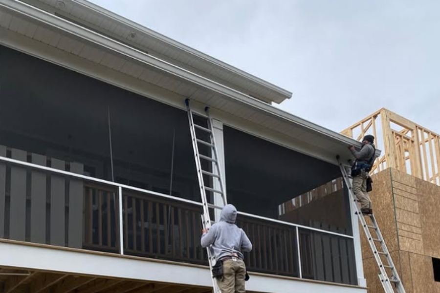 Two gutter installation technicians on ladders installing white seamless gutters on a screened-in porch of a new home in Thunderbolt GA by Spartina Seamless Gutters.
