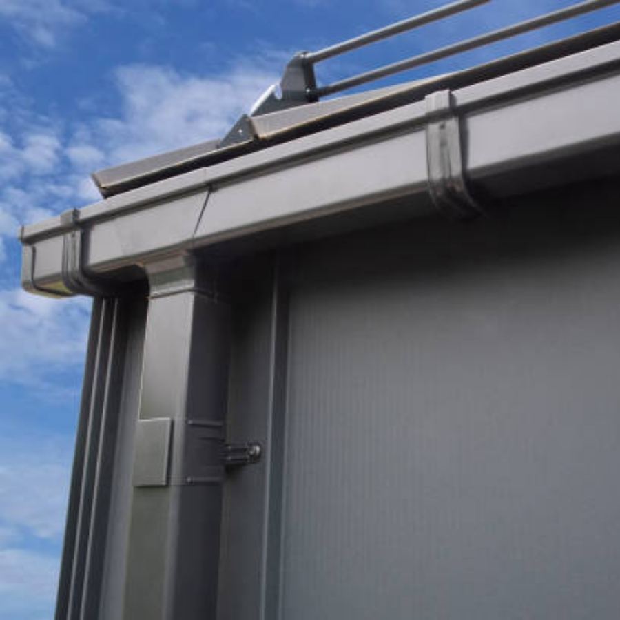 Modern commercial building in Summerville, SC with Spartina seamless gutters and box-style downspout along the metal facade, set against a bright blue sky with scattered clouds.