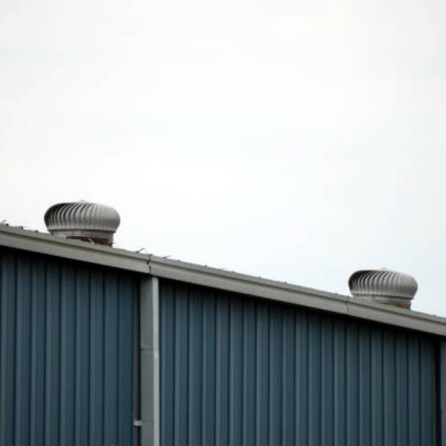 Industrial blue metal building in Sumter, SC with Spartina seamless gutters along the sloped roofline and rooftop turbine vents under an overcast sky.