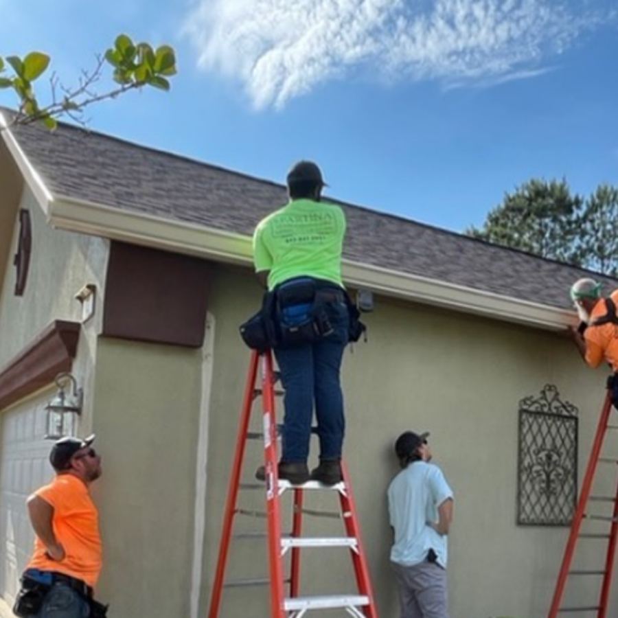 Crew of gutter installers on ladders working on beige stucco home with new white seamless gutters in Whitemarsh Island GA by Spartina Seamless Gutters.